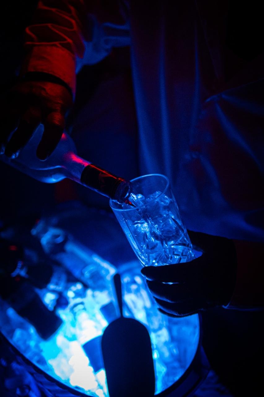 A drink being poured over ice beneath deep blue club light